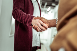 Shaking hands. African American dark-skinned man touching hands of his light-skinned workmate in greeting gesture