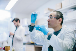 Male doctor examining petri dish at laboratory while coworker working in background